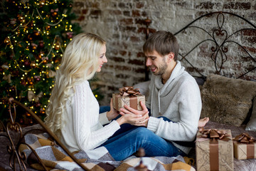 Happy couple of lovers in white pullovers give each other gifts