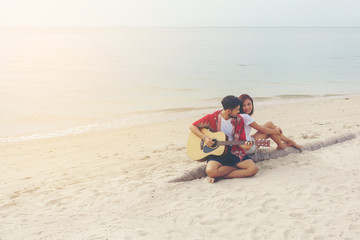 Fototapeta na wymiar Romantic young couple playing a guitar on the beach