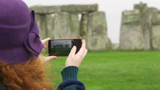 hands of woman holding a smartphone and making a picture to stonehenge 