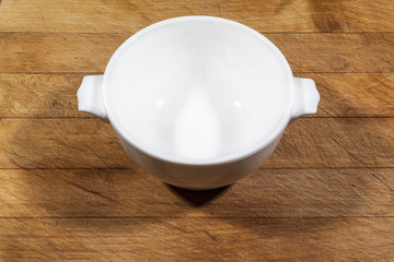 Small white deep bowl with handles on wooden cutting board from side