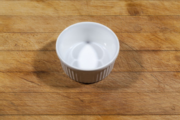 Small white deep bowl on wooden cutting board from side
