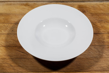 Deep white small soup plate with wide shoulders on wooden cutting board from side
