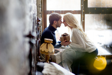 Happy couple of lovers in pullovers give each other gifts sitting