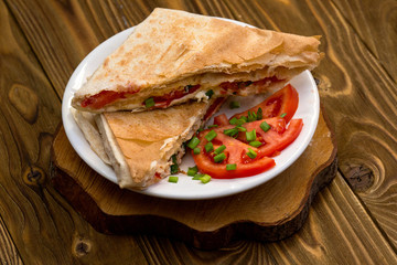 pitabread filled with cheese and vegetables and sauce on wood background