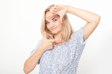 Obraz premium Gesturing finger frame. Beautiful young blond hair woman looking at camera and gesturing finger frame while standing against white background