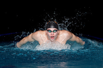 Man in black cap in swimming pool. Butterfly style