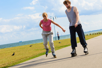 Obraz premium Young pair riding rollerblades in park.