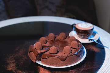 Cappuchino or latte coffe in a white cup on with a cake on a black table.