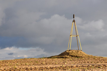 Altitude geodesic mark. The metal structure on the plowed ground on a background of stormy gray sky.