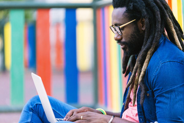 Portrait of african man sitting outside with laptop.