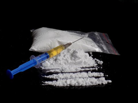 Injection syringe on cocaine drug powder bag, pile and lines on black background