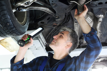 Fototapeta Mechanik, mężczyzna naprawia samochód.Samochód w warsztacie, mechanik sprawdza stan podwozia. obraz