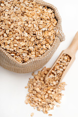Close up burlap sack filled with oat flakes and scoop on white background. Healthy food. Top view, high resolution product