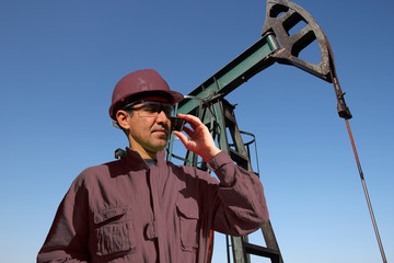 Petroleum Engineer With Cell Phone / Petroleum engineer using mobile phone next to pump jack in the oil field 