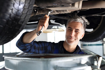 Mechanik samochodowy wymienia  olej silnikowy w warsztacie samochodowym.