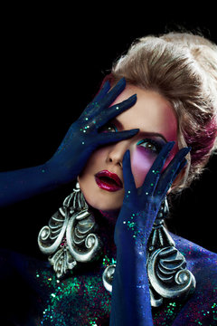 Young attractive blonde girl in bright art-makeup, clasped hands a head. Rhinestones and glitter body painting.