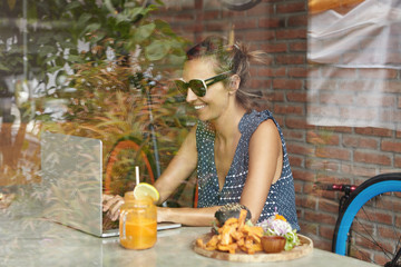 People, technology and communication concept. View from window of happy beautiful Caucasian female writer in shades publishing new article on her blog on internet during lunch at modern coffee shop