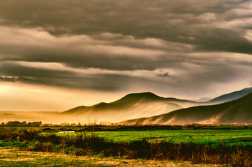 Obraz premium Sunset in green field, mountains, sky and clouds as background