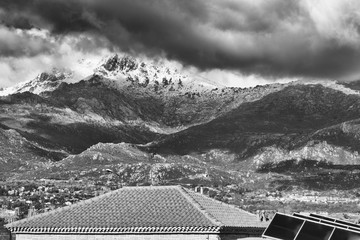 Black and white of Beautiful snow-capped mountains against dramatic clouds and  roof house with solar panel.  Guadarrama mountain range, Madrid, Spain.
