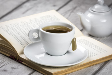 Cup of Tea and Book/ Composition of white cup of tea, cattle and vintage book on white wooden table