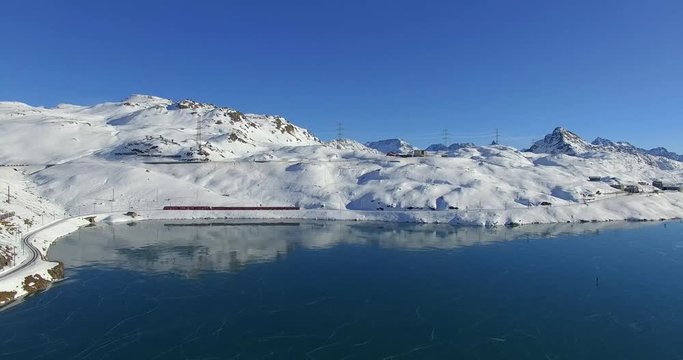 Aerial 4k - Bernina Express - Passo del Bernina - Vista aerea del trenino rosso e del lago Bianco ghiacciato con pattinatori
