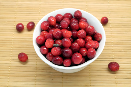 Cranberries in a round white bowl and scattered blueberries on brown straw mat top view
