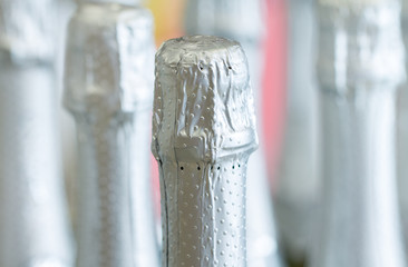 Naklejka na ściany i meble Silver champagne bottle necks and top caps at standing the light background in liquor store.
