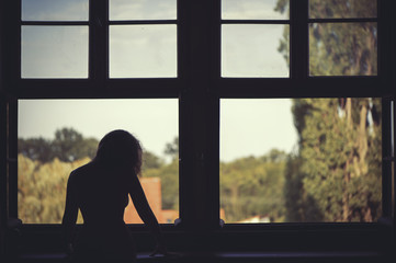 Beautiful naked woman sitting on a window at sunset