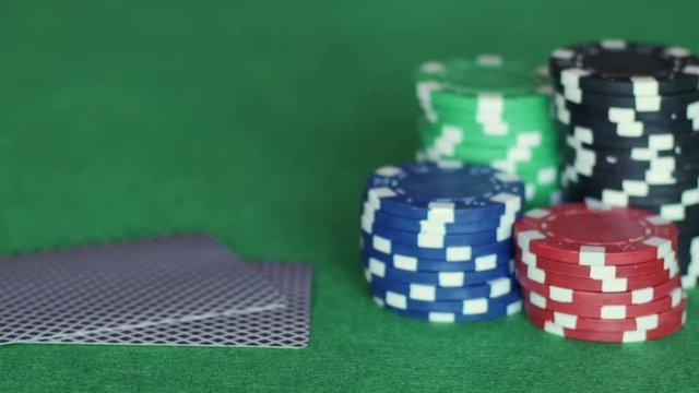 Piles of chips on right and three playing cards are thrown one by one next to them on green table, poker game, gambling. Close up, 4K Ultra HD.