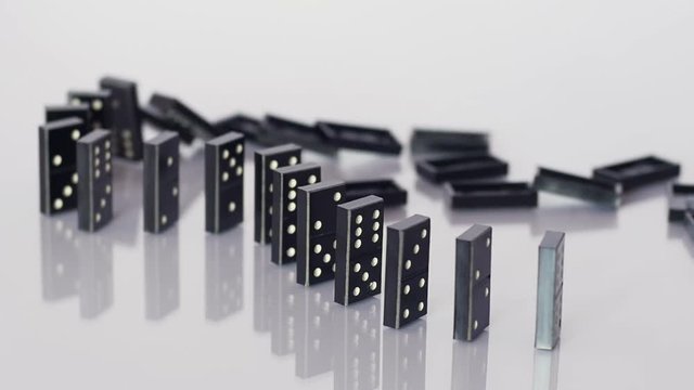 Curved line of dominoes falling in sequence, domino effect, reflective surface, mechanical effect, games. Close up, slow motion.