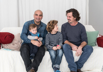 Couple of mature homosexual men sitting on sofa with their two children