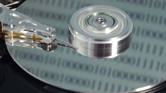 Read-write arm starts and ends rotation of central spindle in hard disk drive, computer binary code runs on reflective surface of magnetic platter. Close up, 4K Ultra HD.