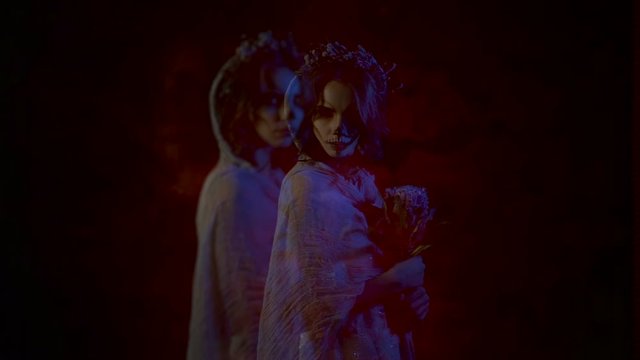 Two ghosts of young dead brides are appearing and staring at the camera. Phantoms of a young women with skull make-up on their faces are silently going by the camera and walking away.