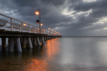 Illuminated wooden pier in Gdynia Orlowo with amazing clouds on the sky.  Poland.