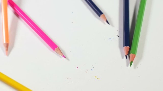 Bunch of colorful pencils falls down on white surface hitting it with their sharp ends and breaking them, concept of brokenness, art supplies. Close up, slow motion.