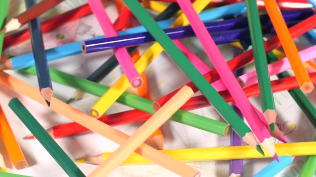 Pile of colorful wooden pencils lying on pictures drawn by children, art for kids, variety, creativity. Closeup, seamless loop, rotation, 4K Ultra HD.