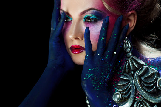Young attractive blonde girl in bright art-makeup, clasped hands a head. Rhinestones and glitter body painting.