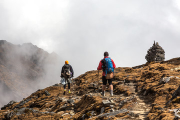 Two Hikers walking on Mountain Slope towards stone Towers