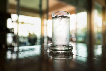 Glass of very cold water in the dark room with sunlight through windows
A glass of cold drinking water on table in restaurant.



