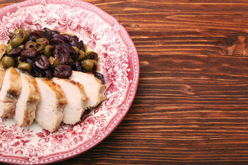 Chicken breasts braised with olives on plate on woden table