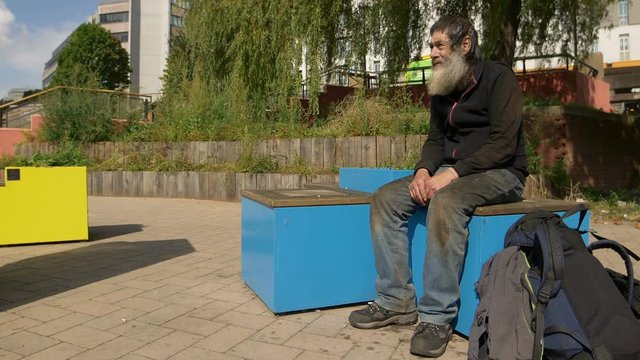 old homeless man sitting in a city square waiting for charity 