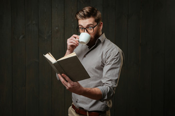 Man in eyeglasses drinking coffee and looking at open book