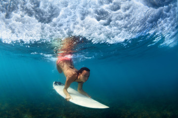 Sportive girl in bikini in action. Surfer with surf board dive underwater under breaking ocean wave. Healthy lifestyle. Water sport, swim, extreme surfing in adventure camp on summer beach vacation