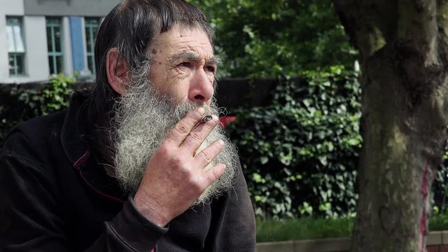old dirty homeless man smoking in the street 
