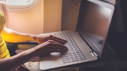 Woman using laptop while is sitting in plane near window.