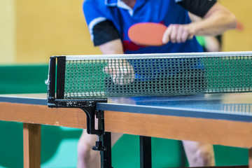 table tennis player serving, focus at the net, player in the background