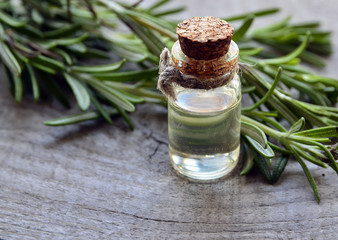 Rosemary essential oil in a glass bottle with fresh green rosemary herb on old wooden table.Rosemary oil for spa,aromatherapy and bodycare.Extract oil of rosemary.Selective focus.