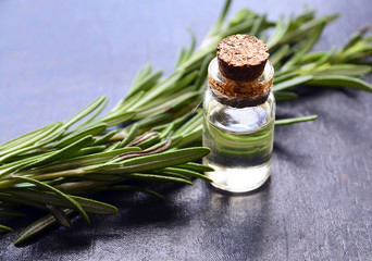 Rosemary essential oil in a glass bottle with fresh green rosemary herb on dark background.Rosemary oil for spa,aromatherapy and bodycare.Extract oil of rosemary.Selective focus.