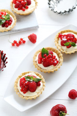 Dessert tartlets with berries on white wooden background