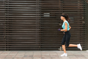 Obraz na płótnie Canvas Side view of sporty young woman running on a sidewalk.